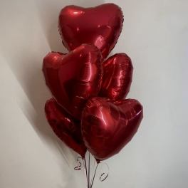 Cluster of red heart-shaped balloons tied with ribbon