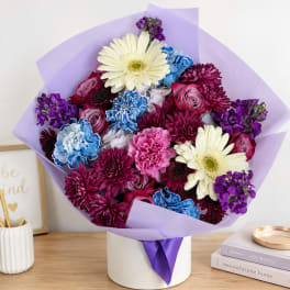 Mixed bouquet of purple, pink, blue, and white flowers in a white box