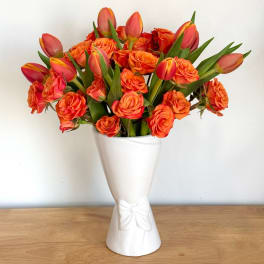 Orange roses and tulips arranged in a white vase