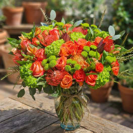 Orange and red bouquet with green accents in a glass vase