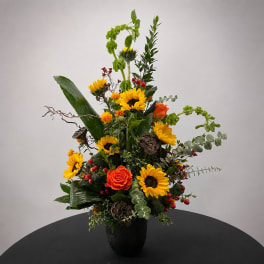 Tall mixed floral arrangement with sunflowers and orange roses in a black vase