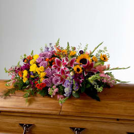 Colorful floral spray on a wooden casket with sunflowers and lilies