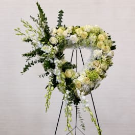 Heart-shaped floral wreath on a stand with white and pale yellow flowers