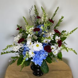 Mixed bouquet in a black vase with white daisies, blue hydrangeas, and red carnations
