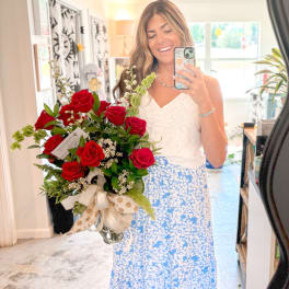 Woman holding a vase of red roses and greenery in a mirror selfie