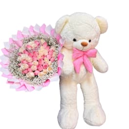 Pink and cream rose bouquet beside a white teddy bear with a pink bow