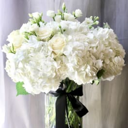 White hydrangea and rose arrangement in a clear glass vase with a black ribbon