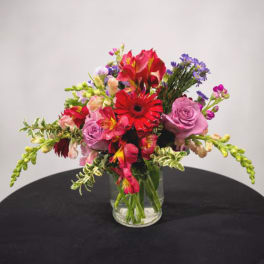 Mixed bouquet of red, pink, and purple flowers in a clear glass vase