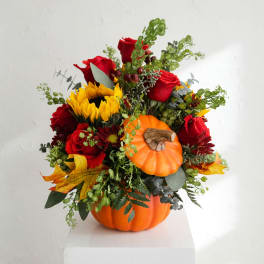 Fall floral arrangement in a pumpkin container with red roses and yellow blooms