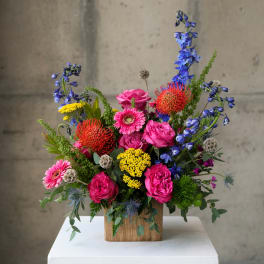 Bright mixed flower arrangement in a wooden box with pink, blue, yellow, and red blooms