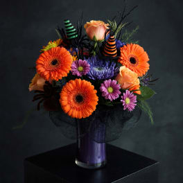 Orange gerbera daisies and roses in a purple vase with Halloween decorations