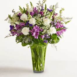 Bouquet of white roses and purple flowers in a tall glass vase