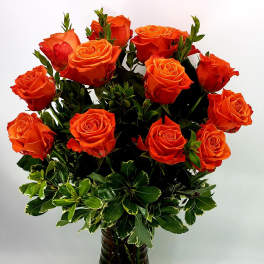 Orange roses arranged in a dark glass vase with variegated greenery