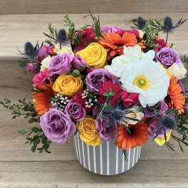 Colorful bouquet of roses, gerbera daisies, and a white anemone in a striped vase