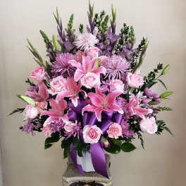 Pink and purple floral arrangement in a white container with a purple ribbon