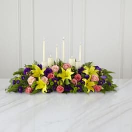 Low floral centerpiece with candles in yellow, pink, and purple