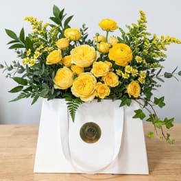 Yellow roses and small yellow filler flowers in a white gift bag