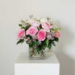 Pink and white roses arranged in a clear square vase