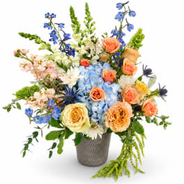 Mixed bouquet of blue, peach, and white flowers in a textured vase