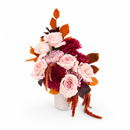 Pink and burgundy flowers arranged in a white vase with orange leaves