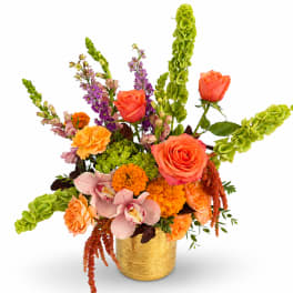 Colorful mixed flower arrangement in a gold vase with roses and orchids