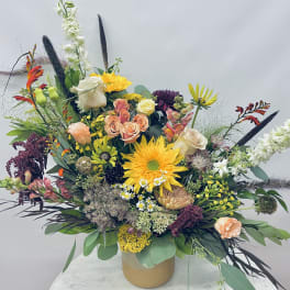 Large mixed floral arrangement in a tan vase with bright yellow and peach blooms