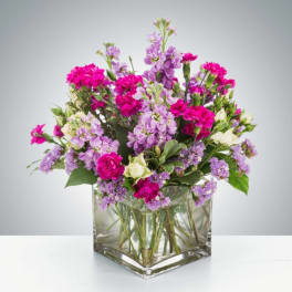 Pink and lavender flowers arranged in a clear square glass vase