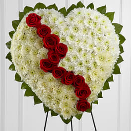 Heart-shaped floral tribute with white flowers and red roses on an easel