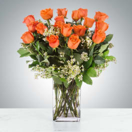 Orange roses in a clear glass vase with small white filler flowers