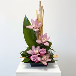 Pink orchids and roses arranged in a black container with bamboo accents