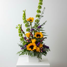 Tall floral arrangement with sunflowers and yellow roses in a white box vase