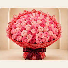 Large bouquet of pink roses wrapped in red paper with a dark ribbon