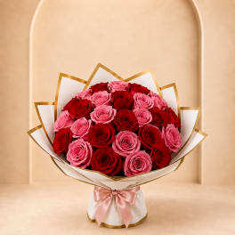 Bouquet of red and pink roses wrapped in white paper with a pink ribbon
