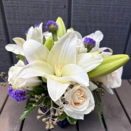 White lilies and cream roses arranged with purple accents in a vase