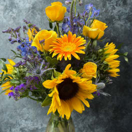 Bouquet of yellow roses, sunflowers, and purple flowers in a glass vase