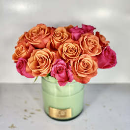 Orange and pink roses arranged in a green round box