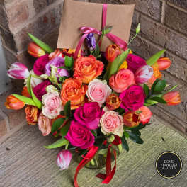 Bright bouquet of pink roses and orange tulips in a glass vase with a kraft card tied with pink ribbon.