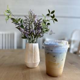 Small purple flower arrangement in a white vase beside an iced drink