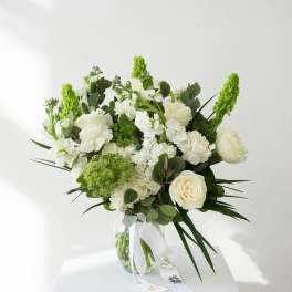 White and green bouquet in a clear glass vase with a ribbon