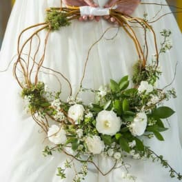 White floral wreath with green foliage and twisting branches held by a person