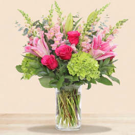 Pink lilies and roses with green hydrangea in a clear glass vase