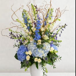 Tall blue and white floral arrangement in a white vase with curly branches