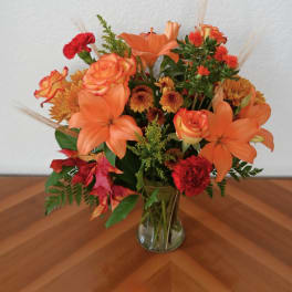 Orange and red mixed flower arrangement in a clear glass vase