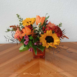 Mixed bouquet in a red glass vase with sunflowers, lilies, and orange blooms