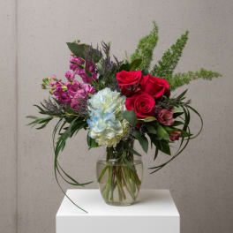 Mixed bouquet of red roses, blue hydrangea, and purple flowers in a glass vase