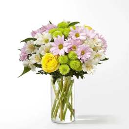 Mixed bouquet of yellow roses, pink daisies, green mums and white alstroemeria in a clear glass vase