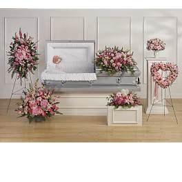 Coordinated pink and white funeral floral set with casket spray, standing sprays, and heart wreath around an open casket
