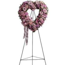 Heart-shaped wreath of pink and lavender roses on a tall black easel with a satin ribbon bow.