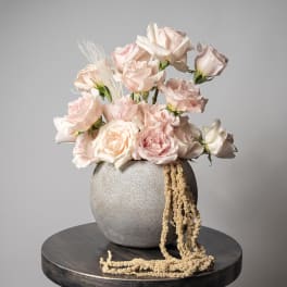 Blush roses arranged in a round gray vase with trailing beige accents
