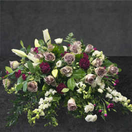 Low floral arrangement with mauve roses, white lilies, and burgundy accents